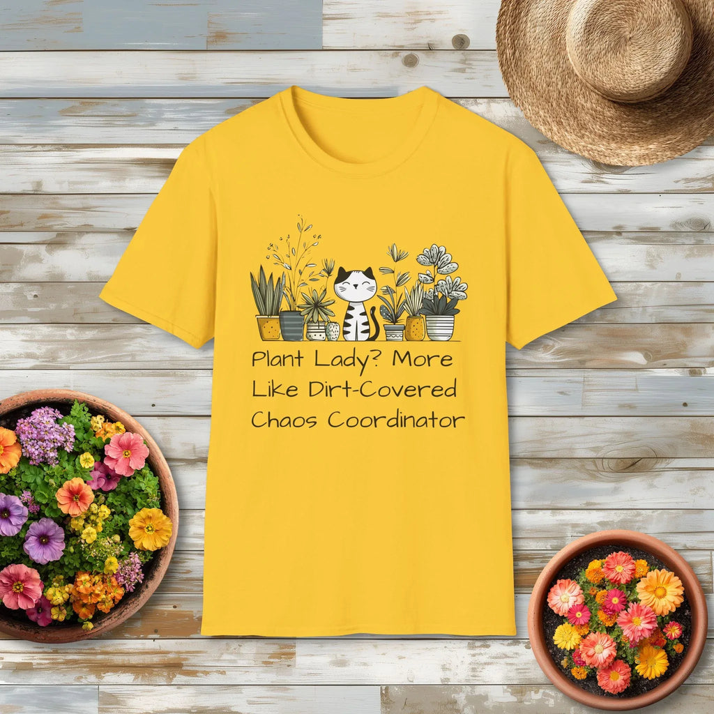 Yellow t-shirt with plant-themed design captioned "Plant Lady? More Like Dirt-Covered Chaos Coordinator" on a wooden surface with potted plant.