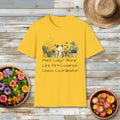Yellow t-shirt with plant-themed design captioned "Plant Lady? More Like Dirt-Covered Chaos Coordinator" on a wooden surface with potted plant.