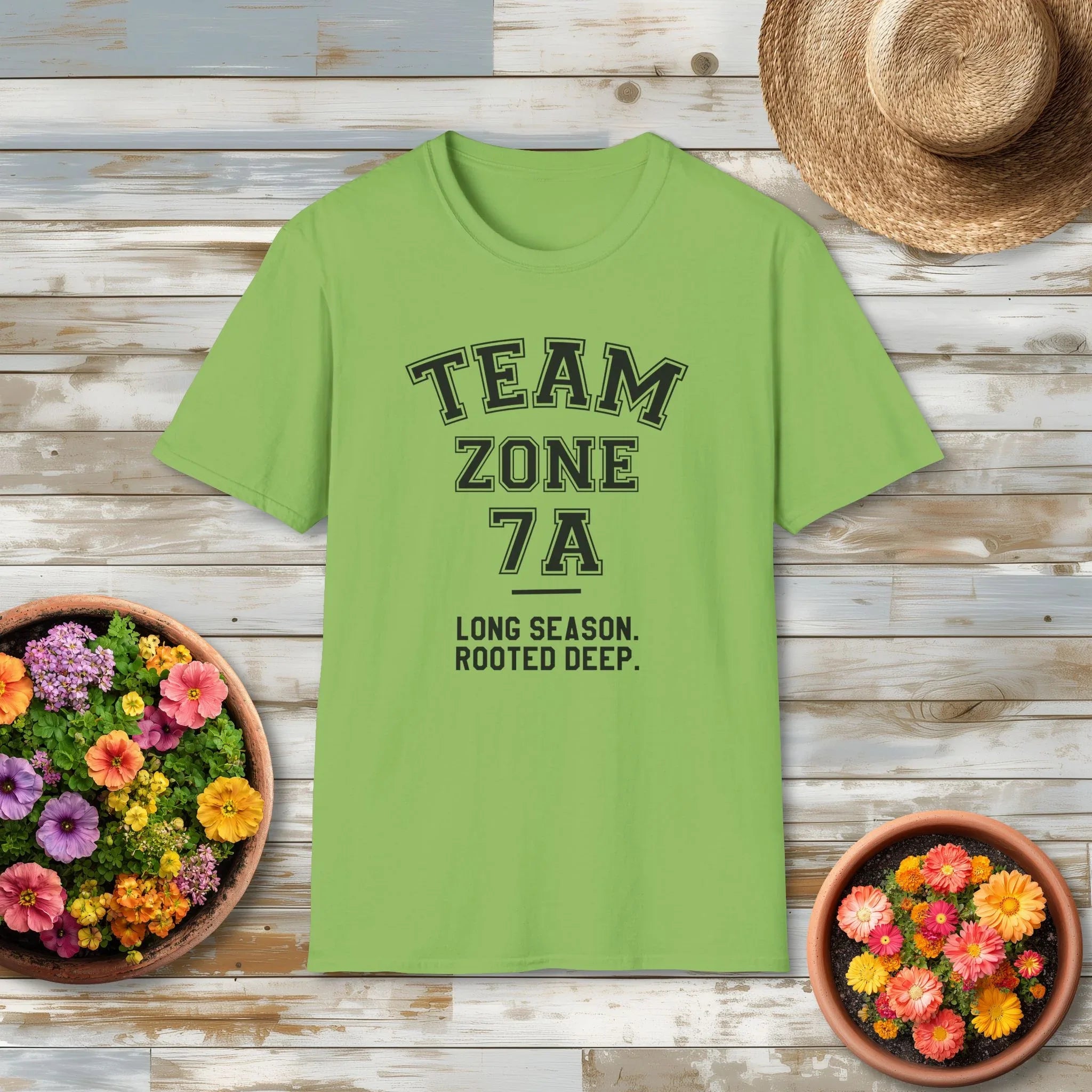 Green t-shirt with text on a wooden surface with flowers and a hat.