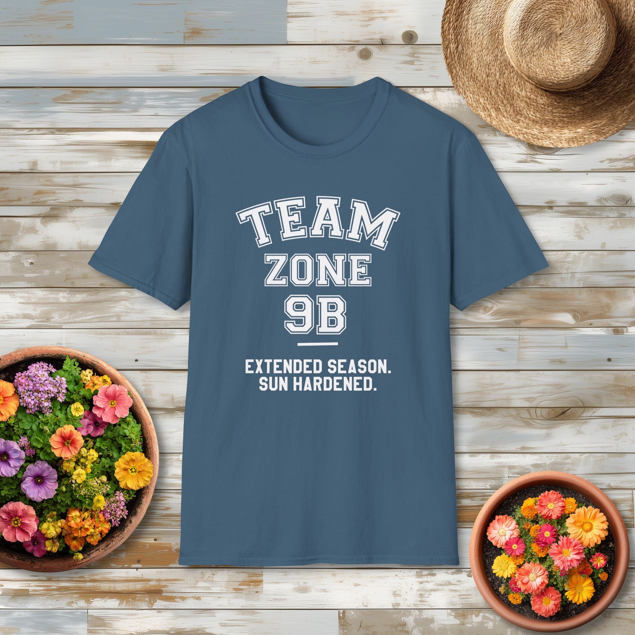 Blue USDA hardiness zone t-shirt with 'Team Zone 9B' text on a wooden surface with flowers and a hat.