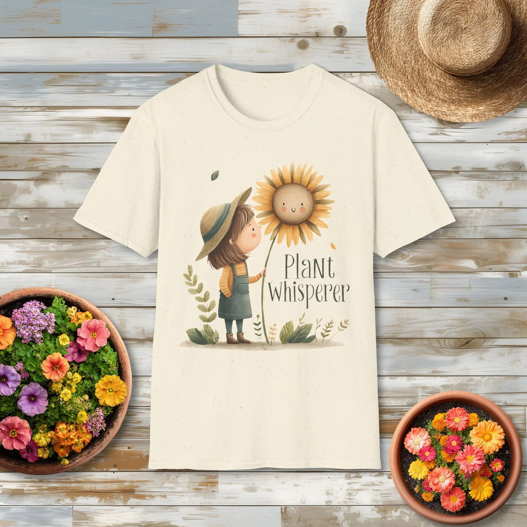 Cream t-shirt with a cottagecore graphic of a girl and sunflower that reads "Plant Whisperer" on a wooden surface with flowers and a hat.