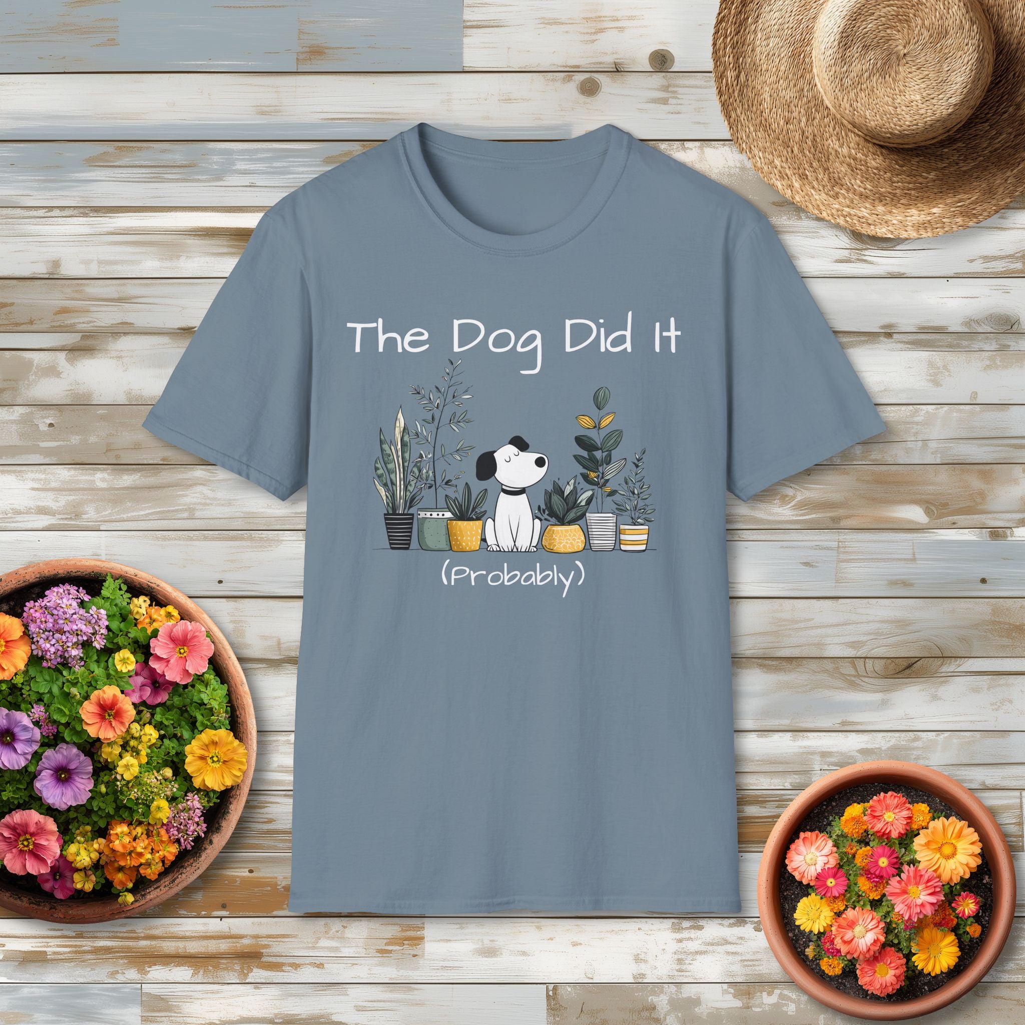 Gray t-shirt with a dog and plant graphic and text on a wooden surface with flowers and a hat.