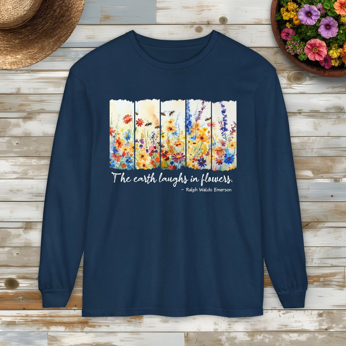 Navy blue sweatshirt with floral design and Ralph Waldo Emerson quote, "The earth laughs in flowers," on a wooden surface