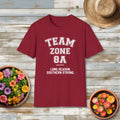 Red t-shirt with 'Team Zone 8A' text on a wooden surface with flowers and a hat.