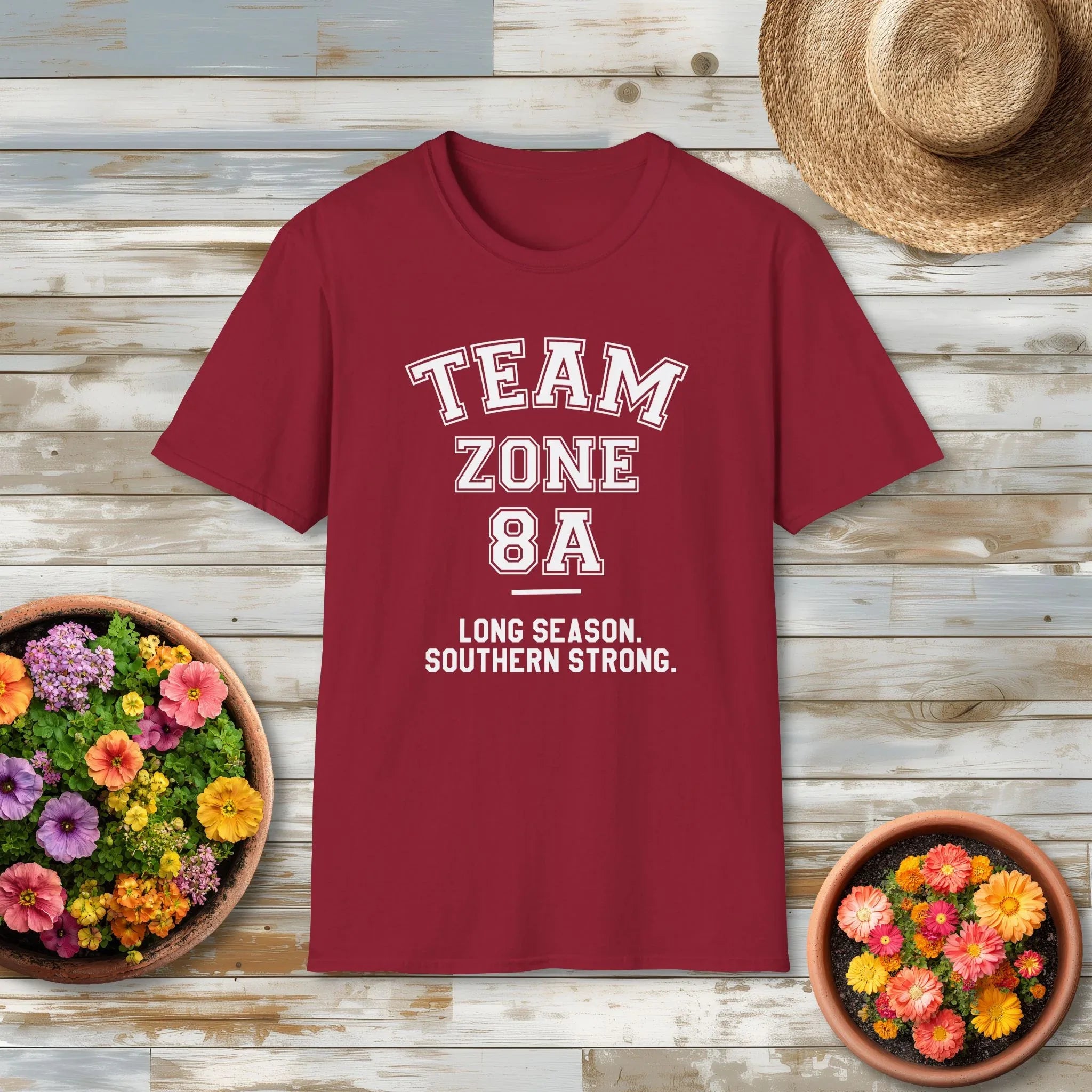 Red t-shirt with 'Team Zone 8A' text on a wooden surface with flowers and a hat.