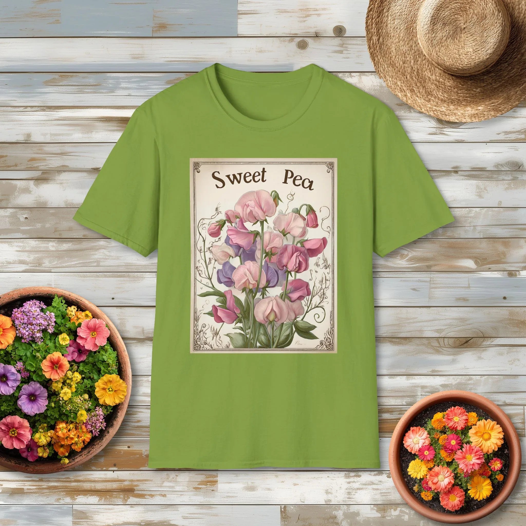 Green t-shirt with 'Sweet Pea' vintage garden art design on a wooden surface with flowers and a hat.