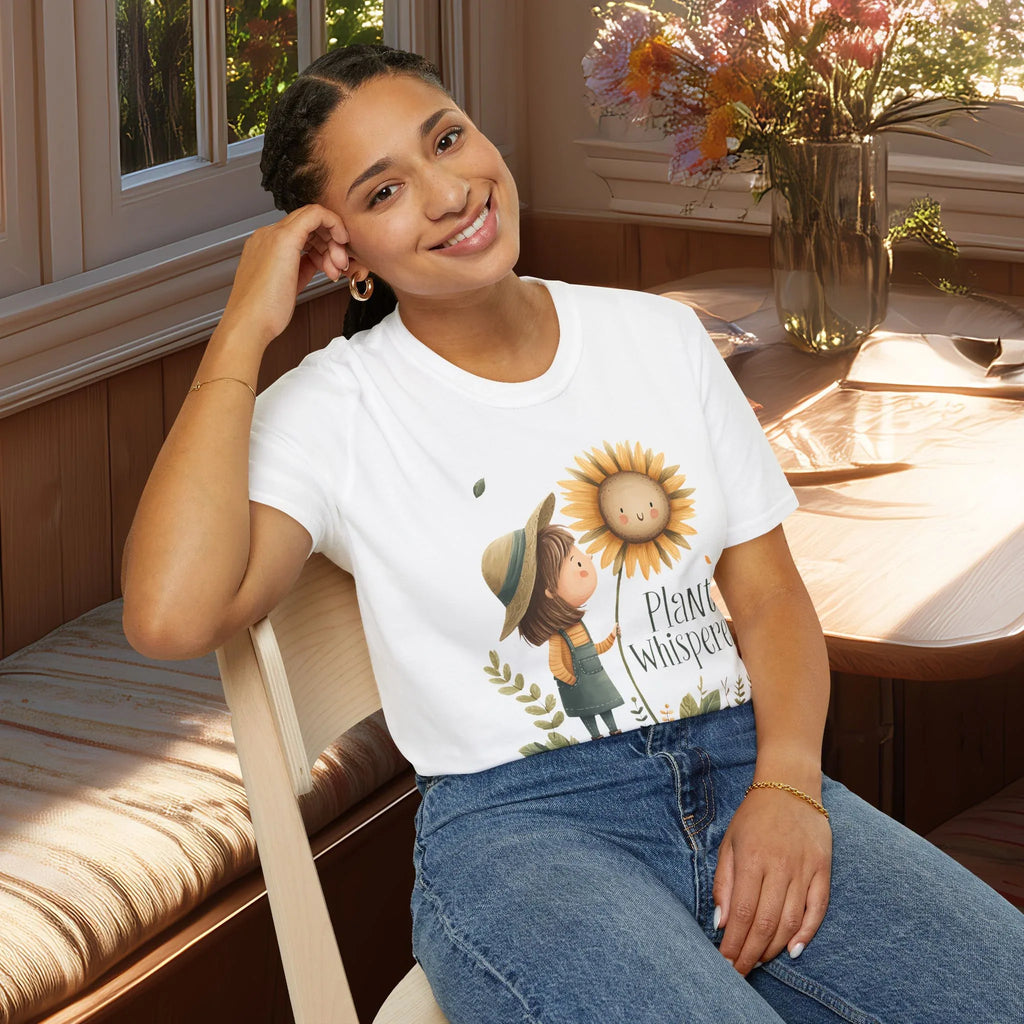 Woman wearing a white t-shirt with a sunflower and girl graphic and text, sitting in a cozy room.