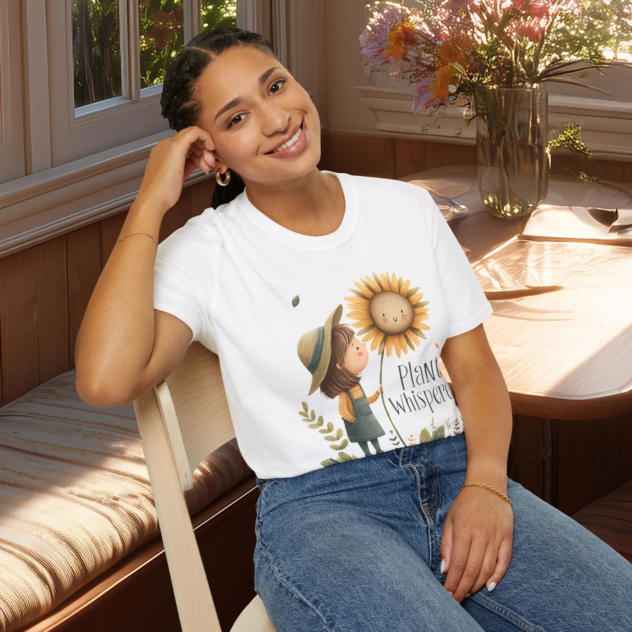 Woman wearing a white t-shirt with a sunflower and girl graphic and text, sitting in a cozy room.